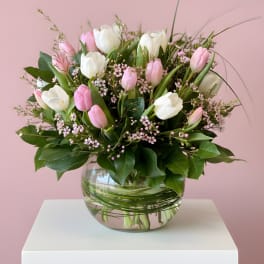 Arrangement of pink and white tulips with tiny pink blossoms in a round clear glass vase