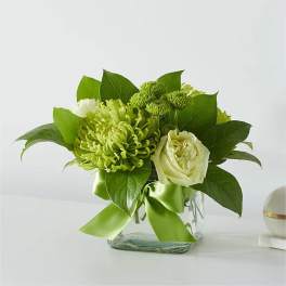 Green and white floral arrangement in a clear glass vase with a ribbon