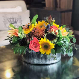 Mixed bouquet of sunflowers, roses, and tropical blooms in a metal container