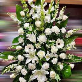 Tall standing spray of white lilies, roses, carnations, and other blooms in an elongated design