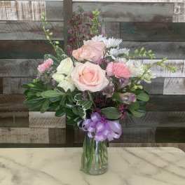 Pink and white flower bouquet in a glass vase with a lavender ribbon