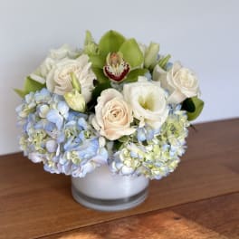 White and pale blue flowers arranged in a low glass vase