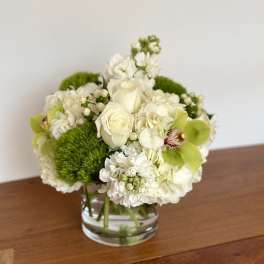 White floral arrangement in a clear glass vase with bright green accents