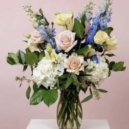 Mixed bouquet of pastel roses, hydrangeas, and blue delphinium in a glass vase