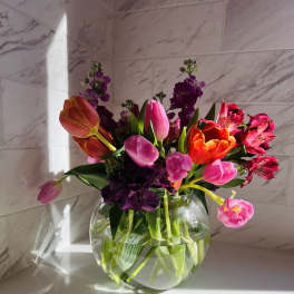 Bright mixed bouquet of tulips and alstroemeria in a round glass vase