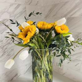 Yellow sunflowers and white tulips in a clear glass vase