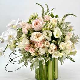 Pastel bouquet of roses, orchids, and calla lilies in a green glass vase