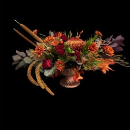 Autumn floral arrangement in a bronze vase with cattails and orange blooms