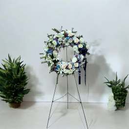 White floral funeral wreath on a stand with blue ribbon