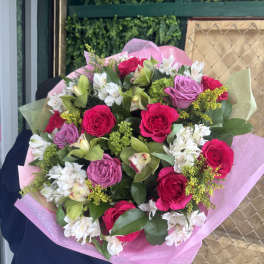 Bouquet of pink roses, white alstroemeria, and green orchids wrapped in pink paper