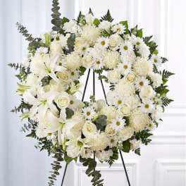 White floral wreath on a black easel with lilies, roses, and daisies