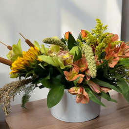 Mixed floral arrangement in a white container with yellow and peach blooms