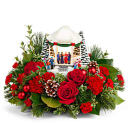 Christmas floral arrangement with red roses and a miniature holiday village centerpiece