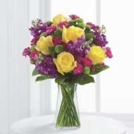Bouquet of yellow roses and purple flowers in a clear glass vase
