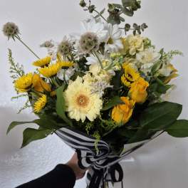 Bouquet of yellow roses, white daisies, and pale blooms wrapped in striped paper