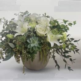White lilies and roses in a round vase with trailing greenery