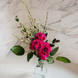 Three hot pink roses in a clear glass vase with small white filler flowers