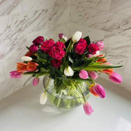 Pink roses and tulips arranged in a clear glass bowl vase