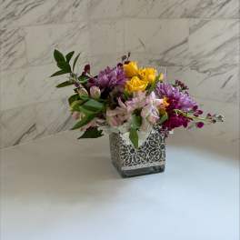Mixed bouquet in a decorative square vase with yellow, purple, and pink flowers