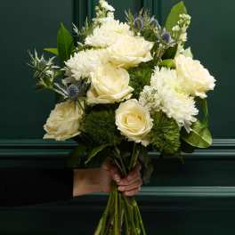 Handheld bouquet of white roses and white chrysanthemums with blue thistle accents