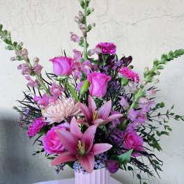 Pink roses and lilies in a white vase with purple accents
