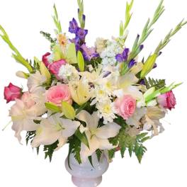 Mixed bouquet of pink roses, white lilies, and purple flowers in a white vase