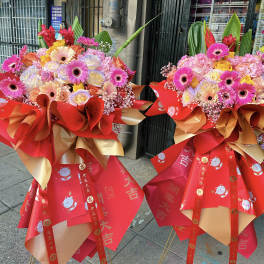 Two bright standing flower arrangements with red and gold wrapping