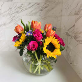 Bouquet of tulips, roses, and sunflowers in a round glass vase