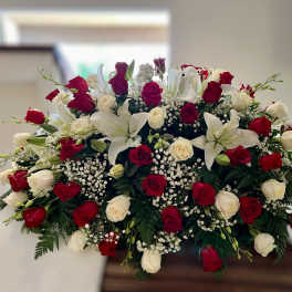 Large red and white rose and lily spray arranged on top of a casket