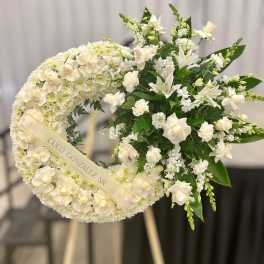 Standing white funeral wreath with roses and lilies on an easel with name ribbon