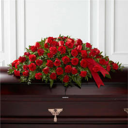 Red rose and carnation casket spray with red ribbons on a dark wood casket