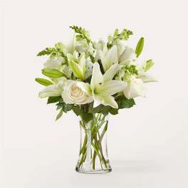 White lilies and roses arranged in a clear glass vase with visible stems.