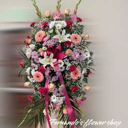 Tall standing spray of pink, white, and peach flowers with a pink ribbon on an easel