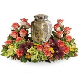 Cremation urn encircled by a low wreath of peach roses, green blooms, and dark purple orchids.