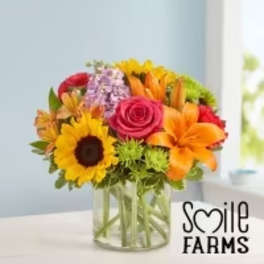 Mixed bouquet in a clear glass vase with sunflowers, roses, and lilies