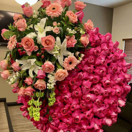 Large circular standing spray of hot pink roses with peach blooms and white lilies on a wooden easel