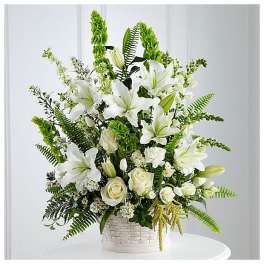 Tall arrangement of white lilies and roses with green Bells of Ireland in a white basket.