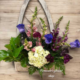 Wall-mounted rustic wooden frame planter with purple roses, white hydrangea, snapdragons, carnations, and green foliage.