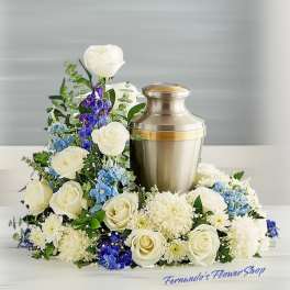 Cremation urn surrounded by white roses, white chrysanthemums, and blue flowers in a low arrangement