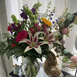 Mixed bouquet with lilies, roses, and purple flowers in a glass vase
