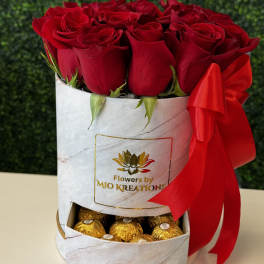 Red roses in a white gift box with gold chocolates and a red ribbon