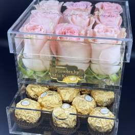 Pink roses in a clear box above gold-wrapped chocolates.