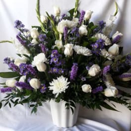 Tall white and purple flower arrangement with roses and mums in a white pot