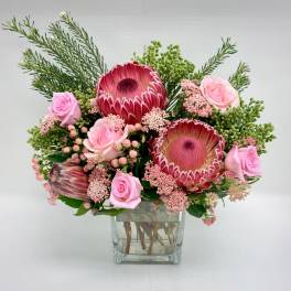 Bouquet of pink protea and roses with filler flowers in a clear glass cube vase