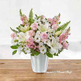 Arrangement of white lilies, daisies, and soft pink roses in a white vase on a wood surface.