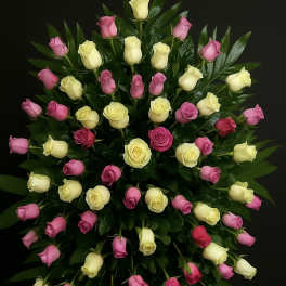 Tall standing spray of pink and pale yellow roses arranged on lush dark foliage