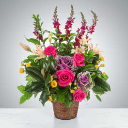 Tall basket arrangement with hot pink roses, lilies, snapdragons, yellow blooms, and purple ornamental cabbage
