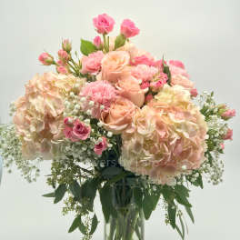 Tall glass vase of blush hydrangeas, pink roses, carnations, and baby’s breath in a soft pastel arrangement