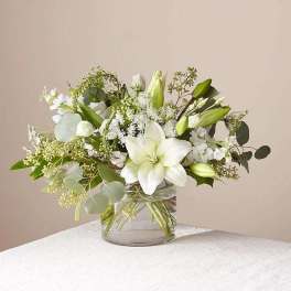 White lilies and delicate white blooms arranged in a clear glass cylinder vase
