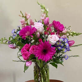 Tall vase arrangement of bright pink gerbera daisies, roses, tulips, and pastel mixed blooms